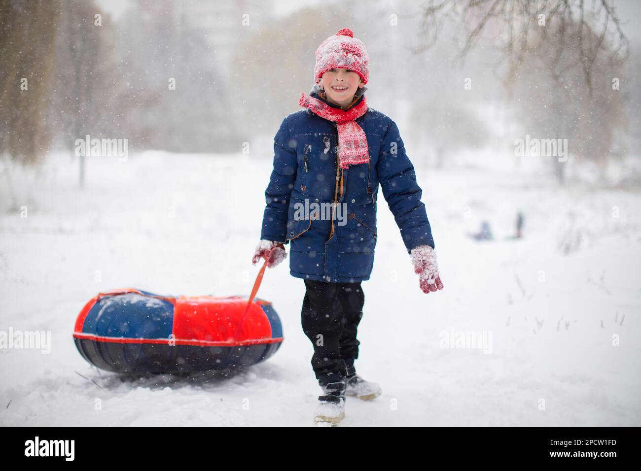 Ein Junge zieht an einem Wintertag einen Schlauchschlitten über den Schnee. Stockfoto