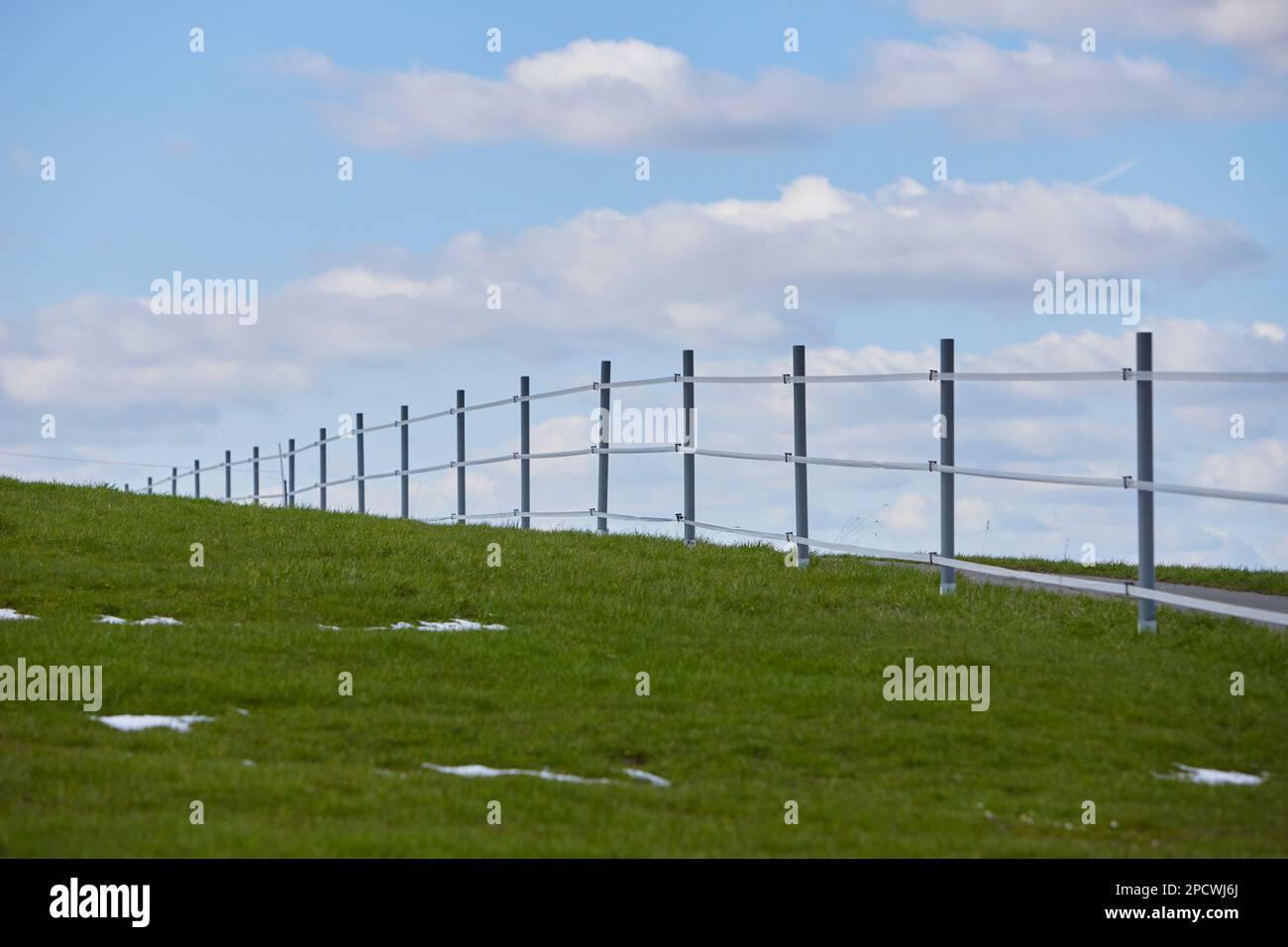 Elektrozaun am Rande einer Wiese, kleine Schneepunkte auf dem Gras Stockfoto