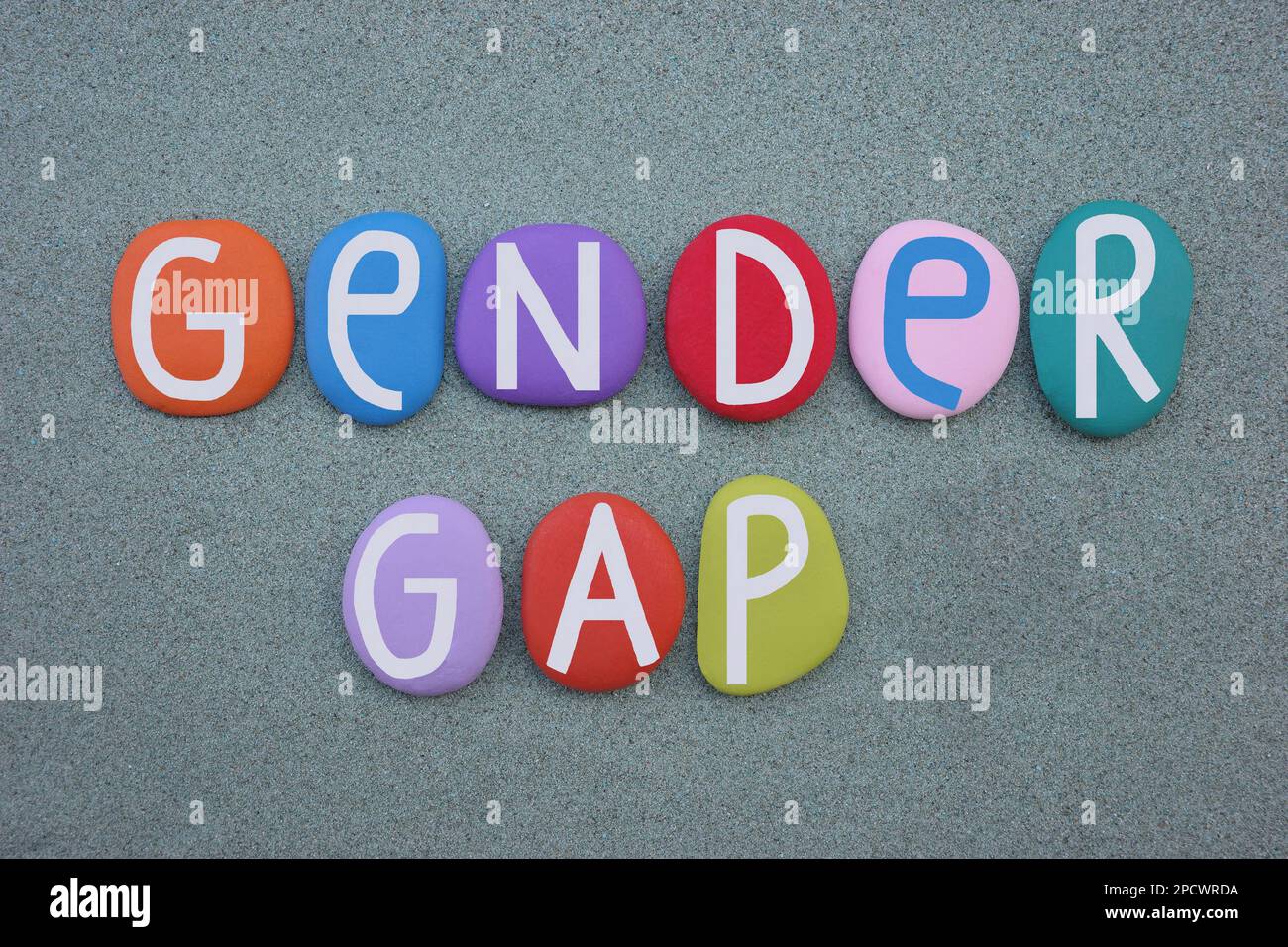 Gender Gap, Slogan für soziale Themen, mit handgemalten, mehrfarbigen Buchstaben auf grünem Sand Stockfoto