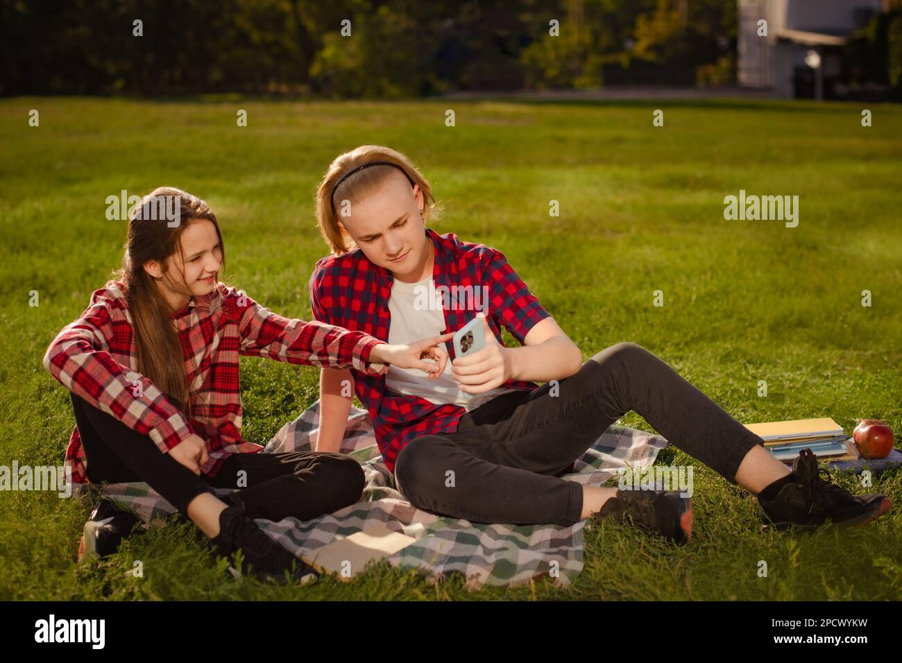 Teenager Mädchen und Junge lernen und diskutieren Hausaufgaben nach Unterricht auf Grünrasen im Schulhof Stockfoto