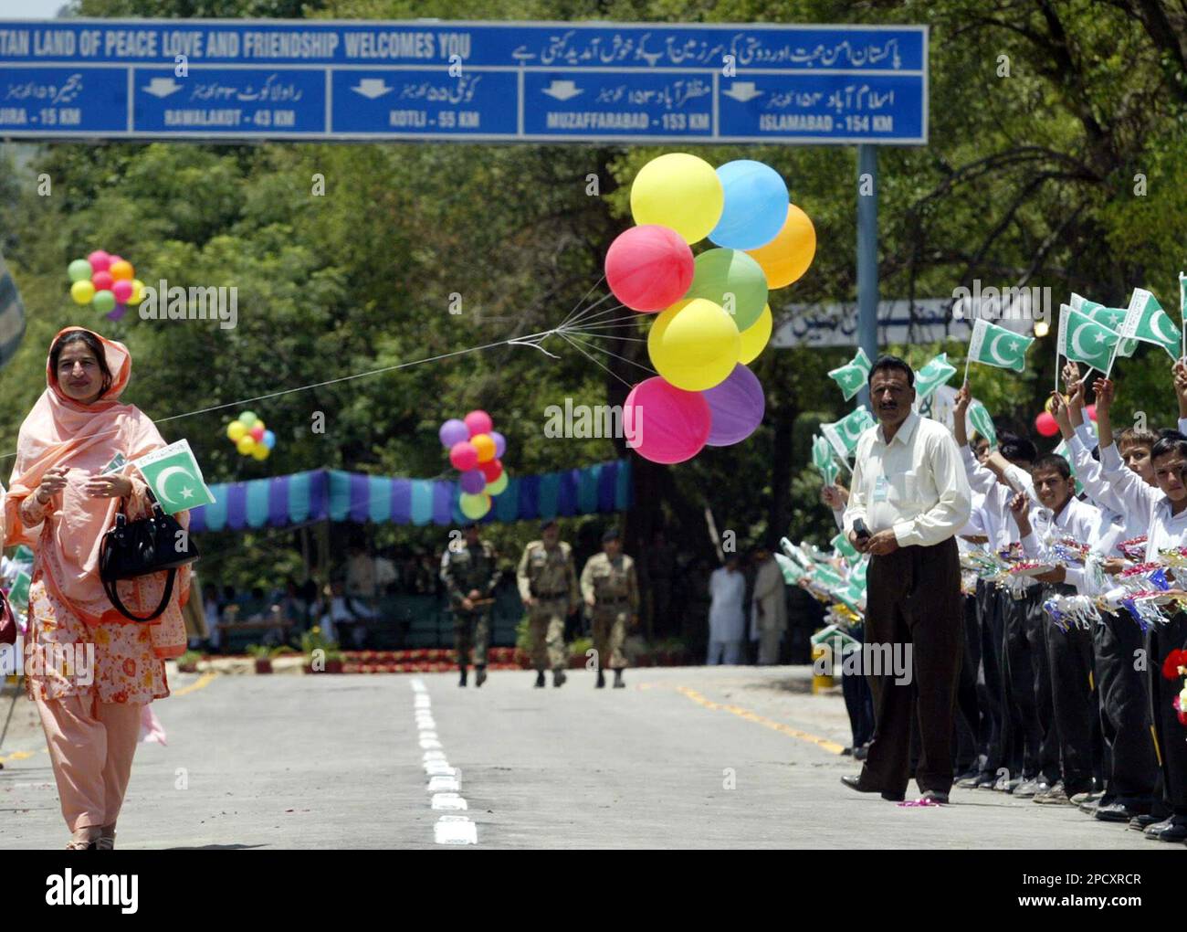 A passenger, left, crosses over to India from Pakistani side of Kashmir, as children wave flags at Chakka Da Bagh, in Poonch district, 250 kilometers (156 miles) northwest of Jammu, India, Tuesday, June 20, 2006. Scores of people cheered and waved flags as Indian authorities on Tuesday flagged off a second bus service linking Indian border town of Poonch to Rawalkhot, in the Pakistan-controlled portion of Kashmir. (AP Photo/Channi Anand) Stockfoto