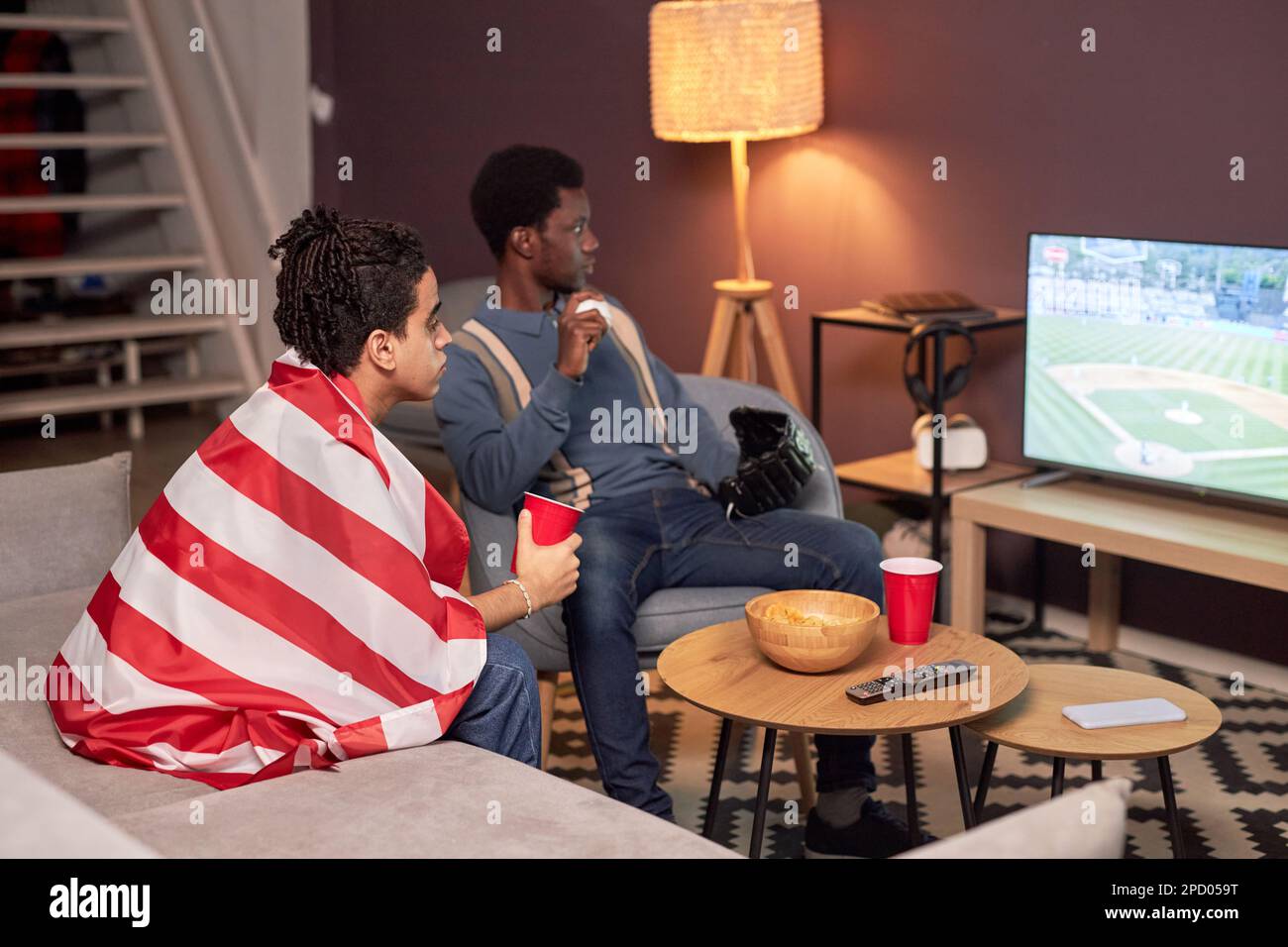 Porträt von zwei Freunden, die sich im Wohnzimmer ein Sportspiel im Fernsehen ansehen und Bier trinken Stockfoto