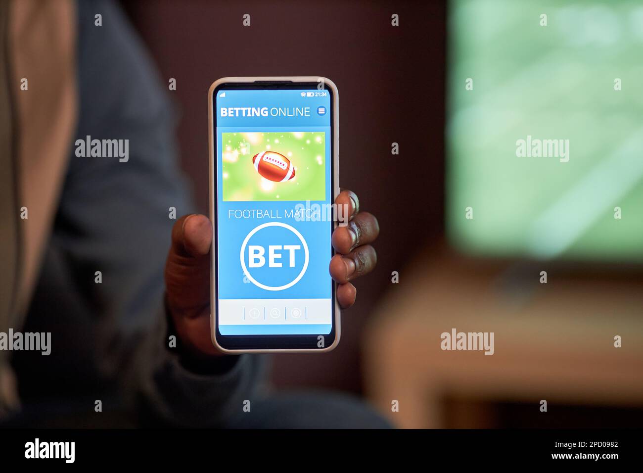 Nahaufnahme eines männlichen Smartphones mit Sportwetten-App in die Kamera, während er sich zu Hause ein Fußballspiel ansieht, Kopierraum Stockfoto