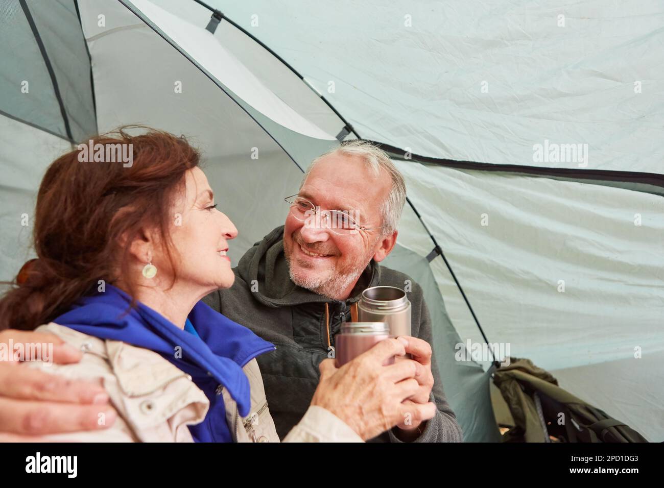 Glückliches älteres Paar, das während des Urlaubs im Campingzelt zusammen Tee trank Stockfoto