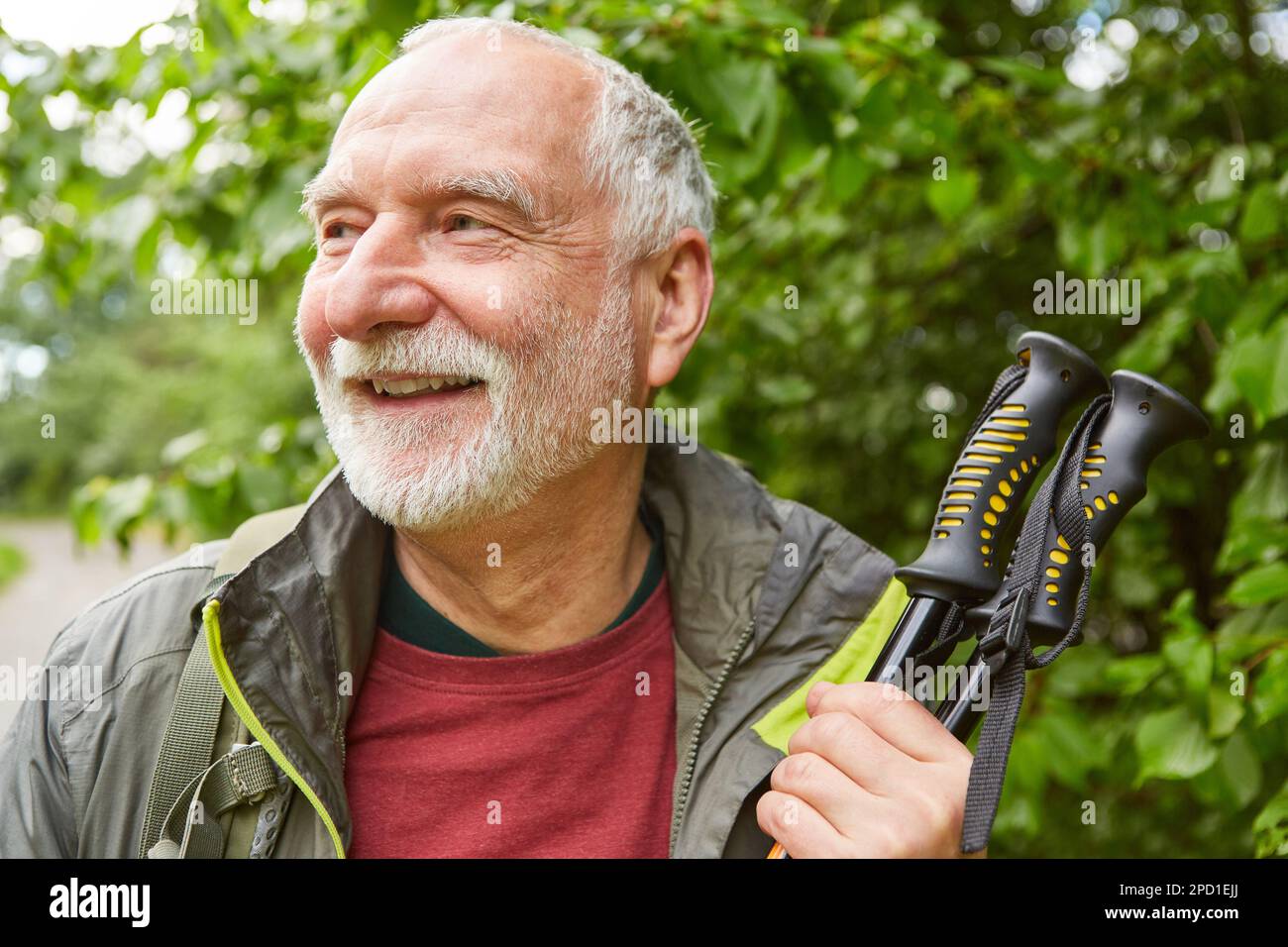 Lächelnder Seniorenmann mit Wanderstöcken im Jackett, der während des Urlaubs wegblickt Stockfoto