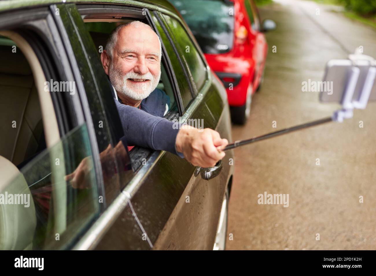 Lächelnder Senior-Mann, der Selfie mit dem Smartphone macht, während er im Urlaub im Auto unterwegs ist Stockfoto