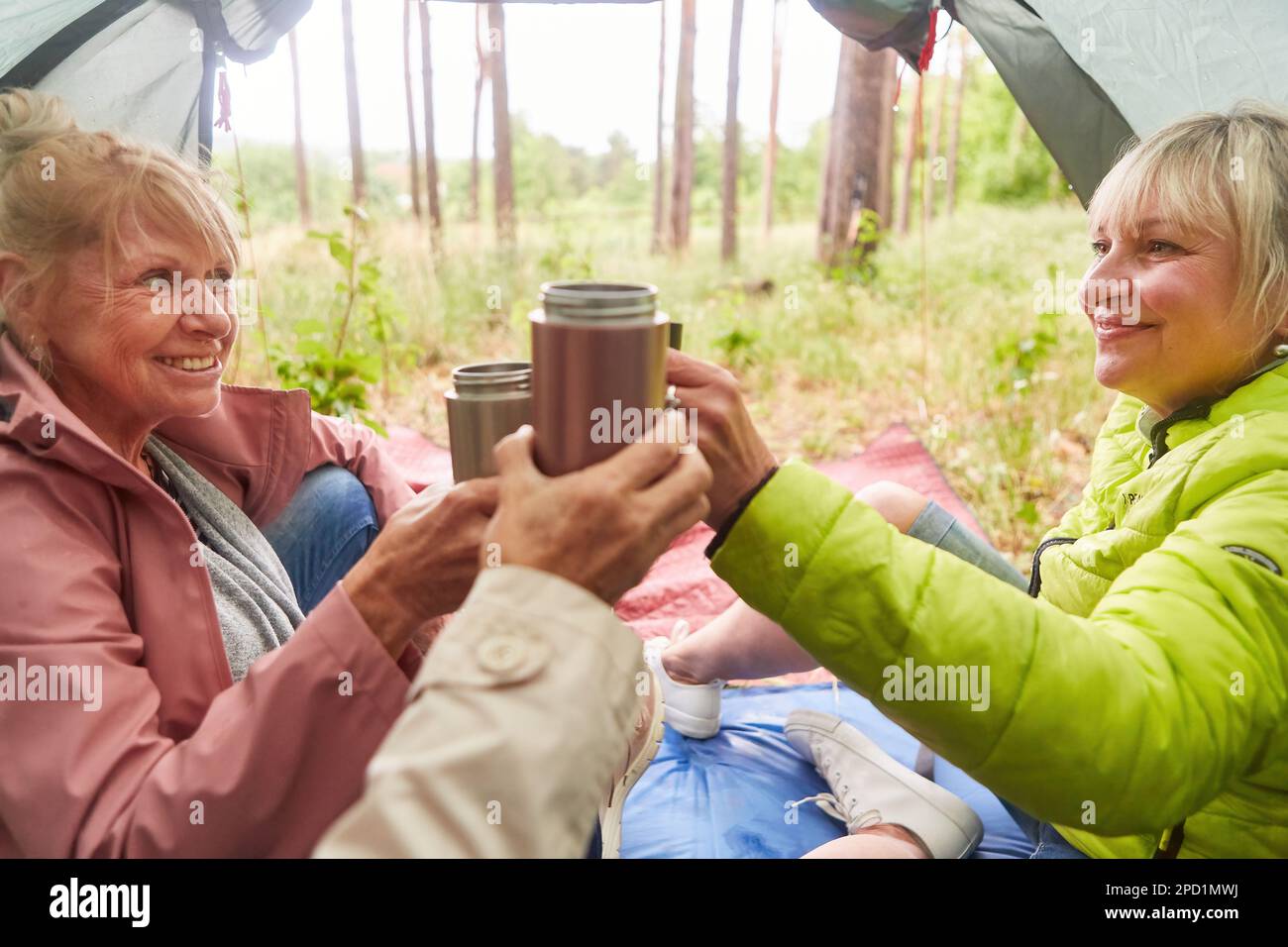 Lächelnde Seniorinnen, die Teetassen toasten, während sie im Urlaub im Wald campen Stockfoto