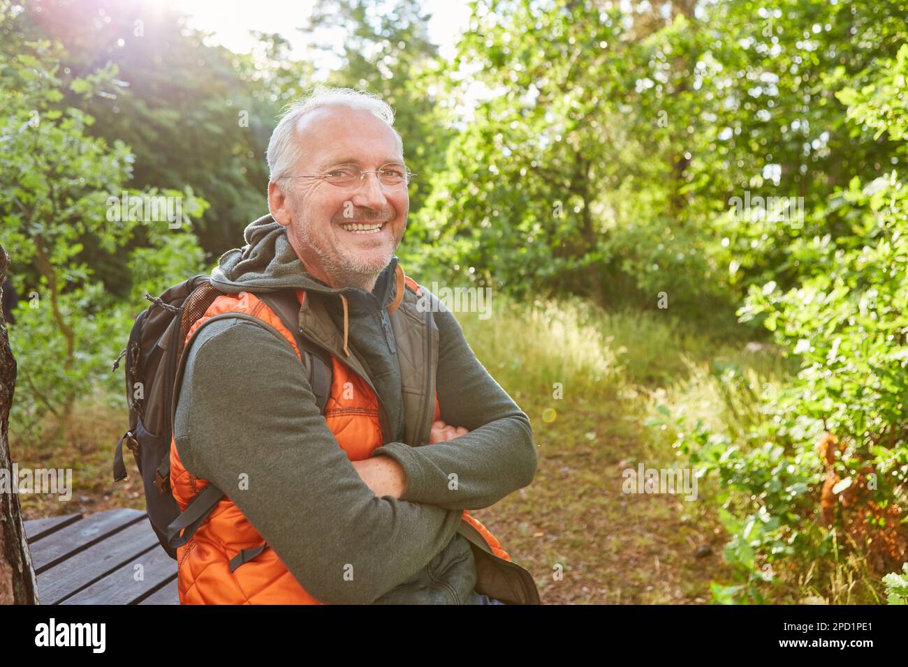 Porträt eines glücklichen Seniorenmannes, der im Sommer mit gekreuzten Armen im Wald sitzt Stockfoto
