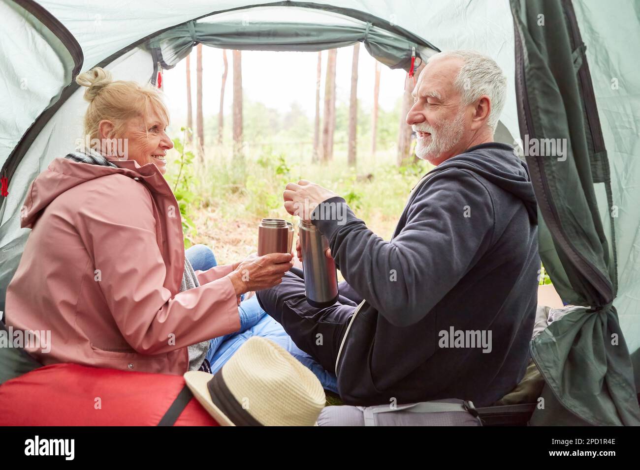 Lächelndes Seniorenpaar, das zusammen Tee trank, während es während des Ausflugs im Wald im Zelt saß Stockfoto