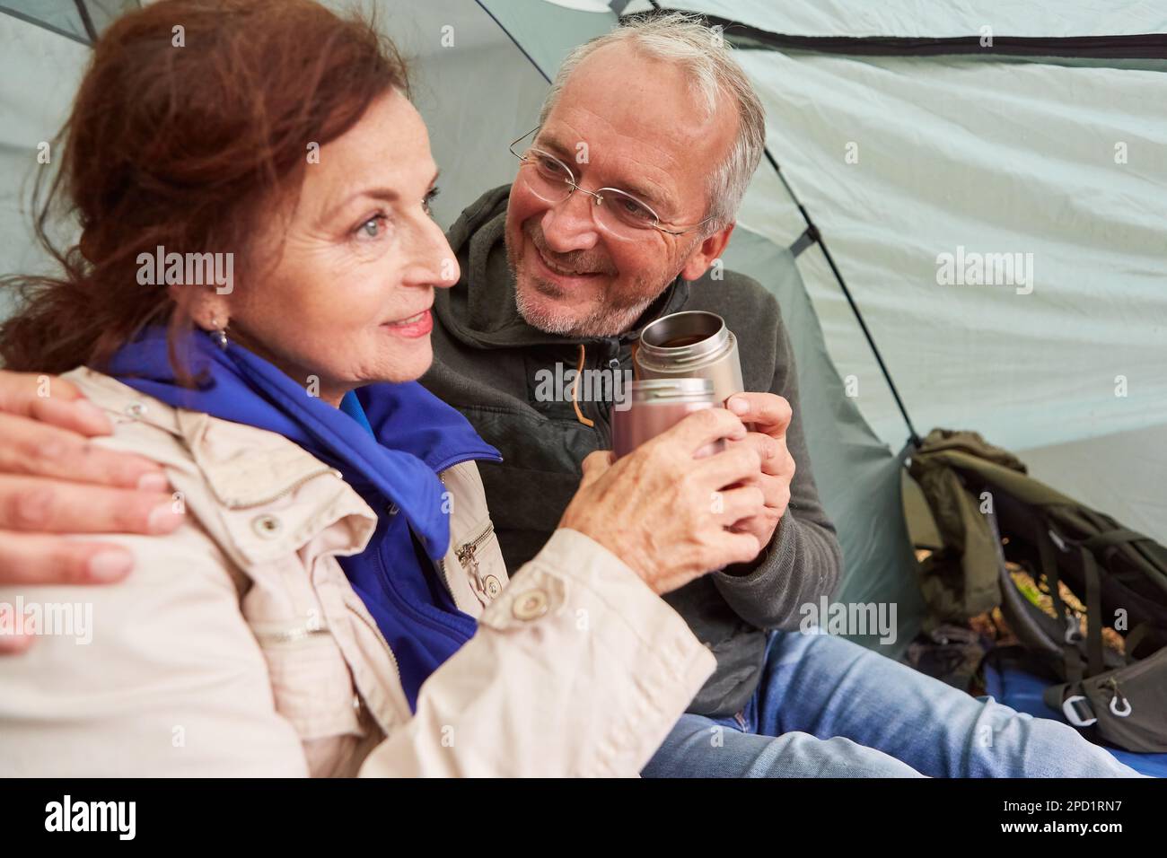 Lächelnder Senior-Mann, der eine Frau ansieht, während er beim Camping Tee im Zelt trinkt Stockfoto
