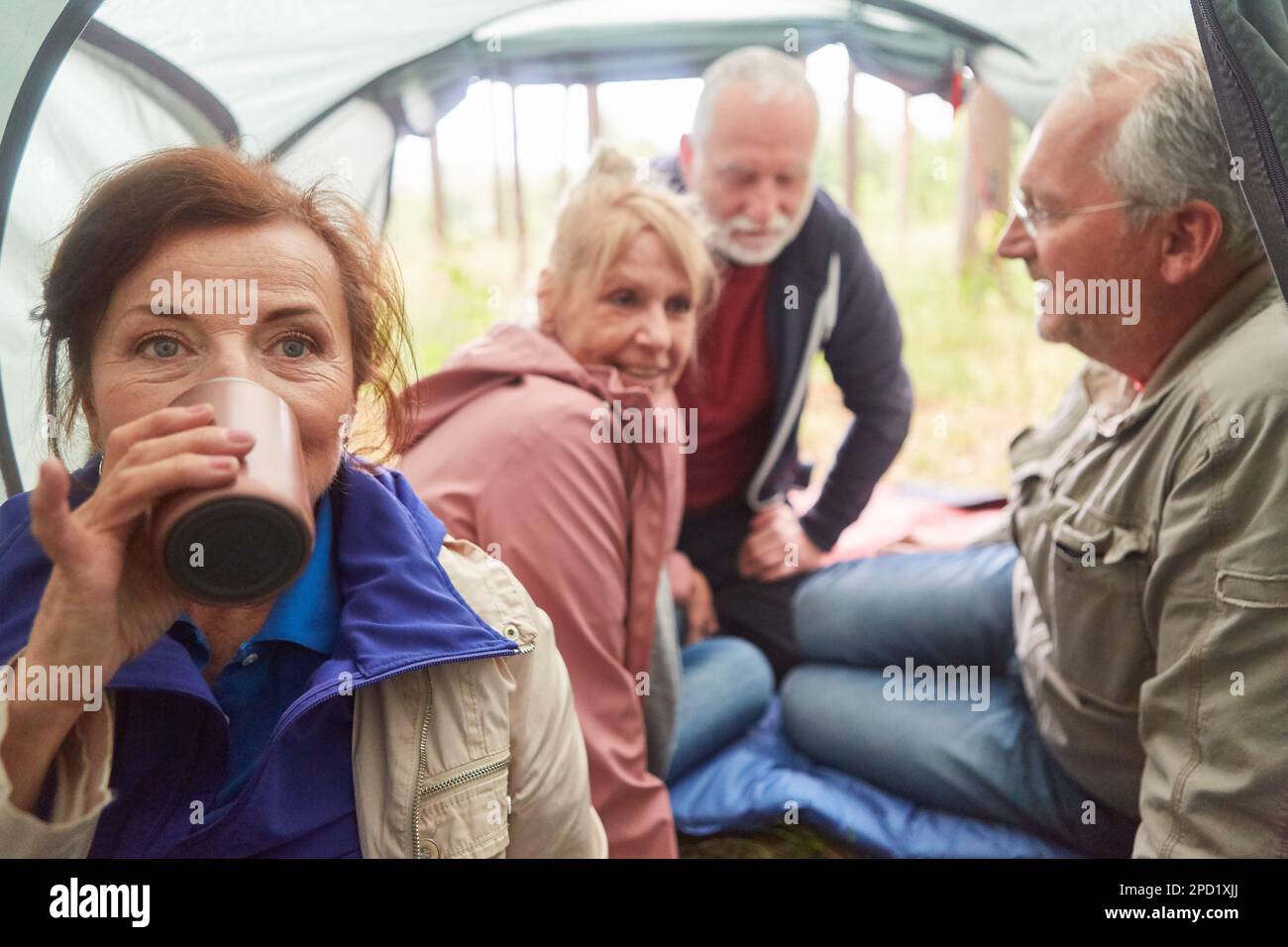 Porträt einer älteren Frau, die Tee mit männlichen und weiblichen Freunden im Hintergrund im Zelt trinkt Stockfoto