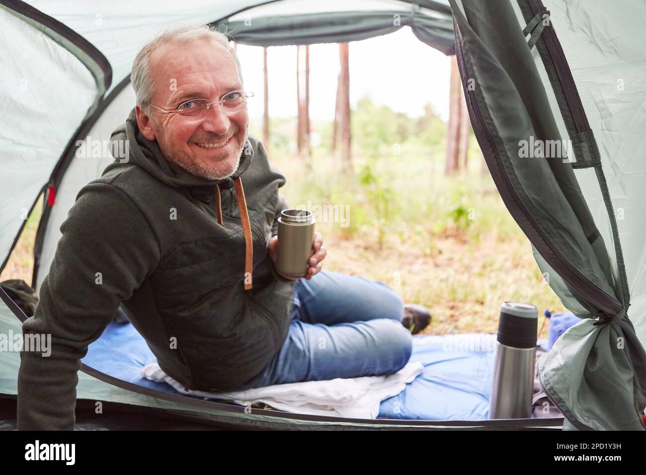 Porträt eines lächelnden Seniorenmannes mit isoliertem Getränkebehälter im Zelt Stockfoto