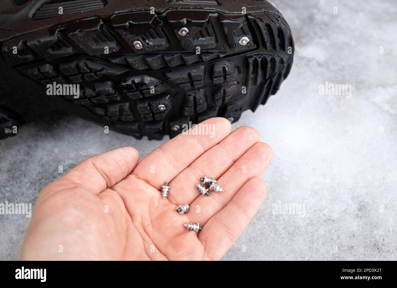 Person zeigt die selbstschraubenden Stollen, die an der Winterstiefelsohle befestigt sind. Anti-Rutsch-Konzept für den Winter. Draußen auf einer eisigen Straße. Reifenbolzen für Stiefel. Stockfoto