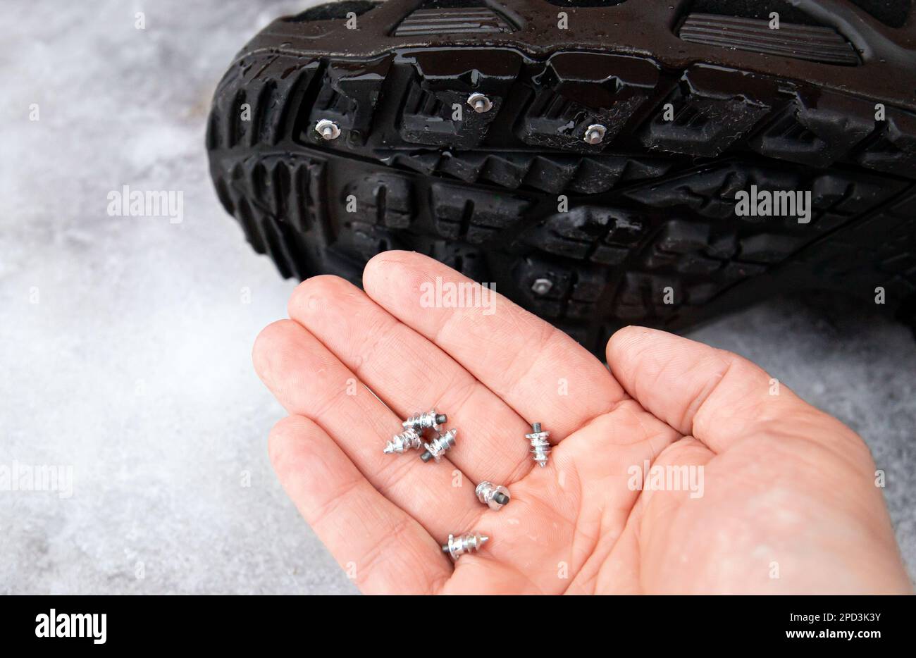 Person zeigt die selbstschraubenden Stollen, die an der Winterstiefelsohle befestigt sind. Anti-Rutsch-Konzept für den Winter. Draußen auf einer eisigen Straße. Reifenbolzen für Stiefel. Stockfoto