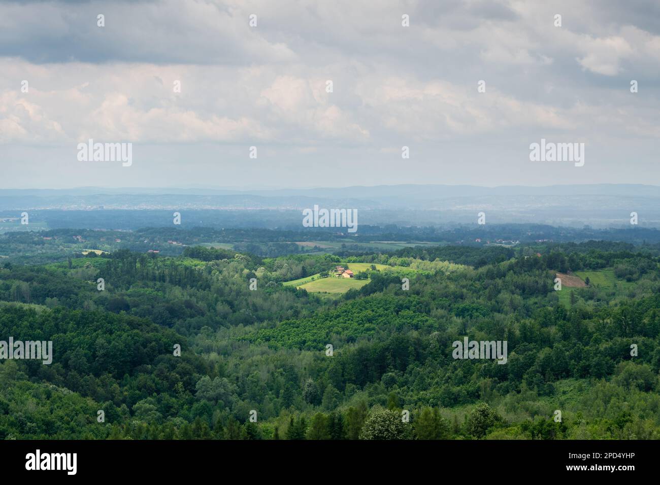 Hügelige Landschaft mit üppigen Wäldern an bewölkten Tagen, Landschaft mit Sonnenflecken auf verstreuten Dörfern und fernen Hügelsilhouetten in Nebel Stockfoto