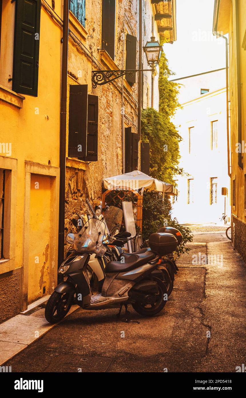 Italienische Häuser mit Fensterläden und Motorrädern. Sonniger Tag im historischen Zentrum von Verona. Blick auf die Straße. Stockfoto