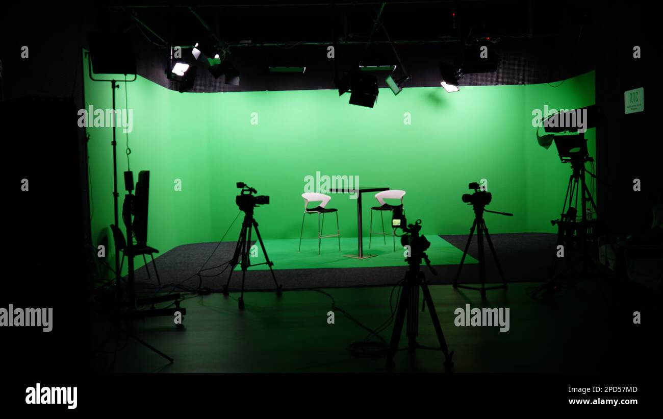 Moderne Einrichtung im Chroma Key Studio mit Fernseher, grünem Bildschirm, Licht, Kameraausstattung und Möbeln. Schießstudio mit Gastgeber und professioneller Ausrüstung. Stockfoto