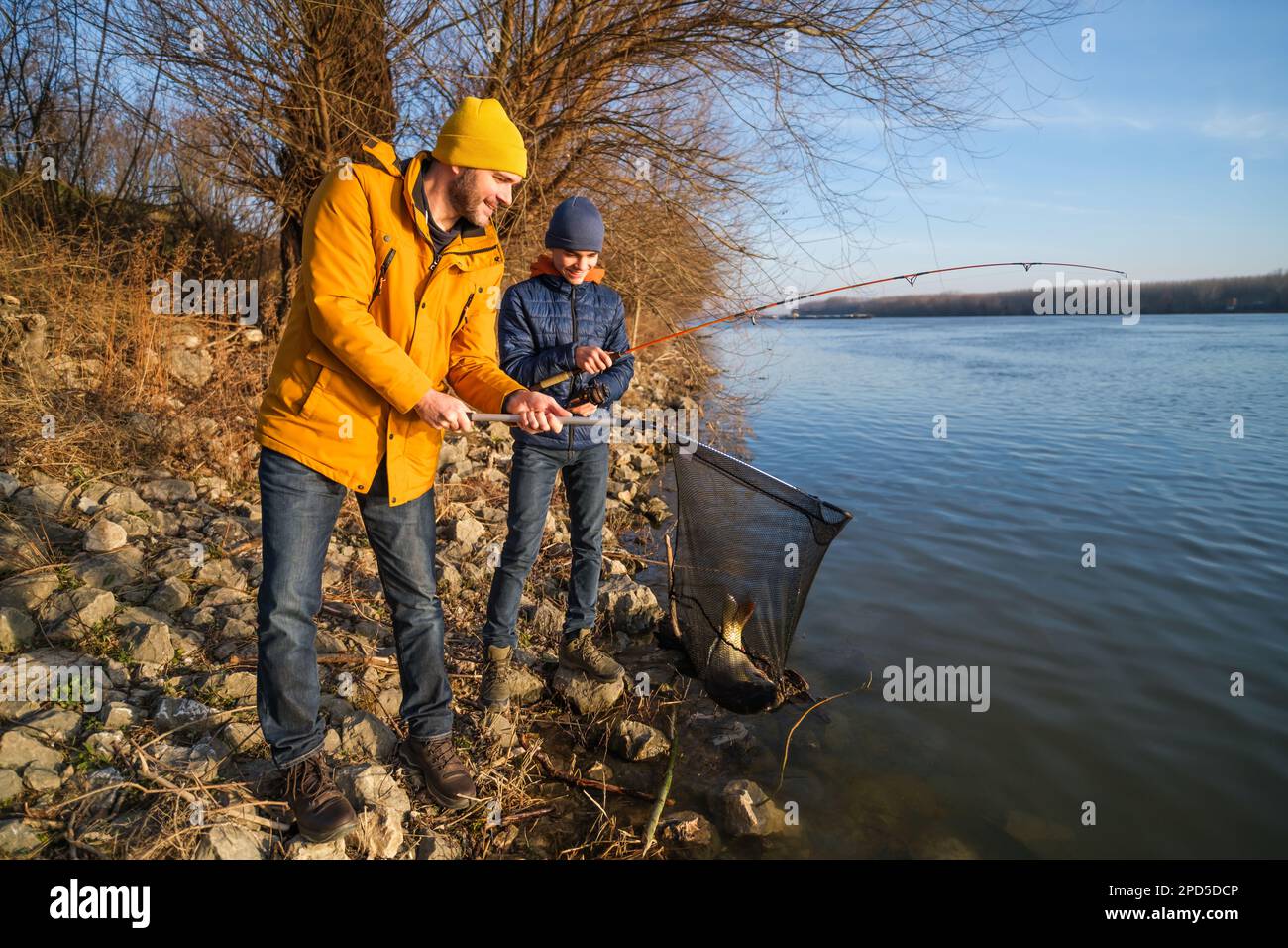 Vater und Sohn fischen an sonnigen Wintertagen. Sie haben einen Fisch gefangen und halten ihn in einem Landenetz. Stockfoto