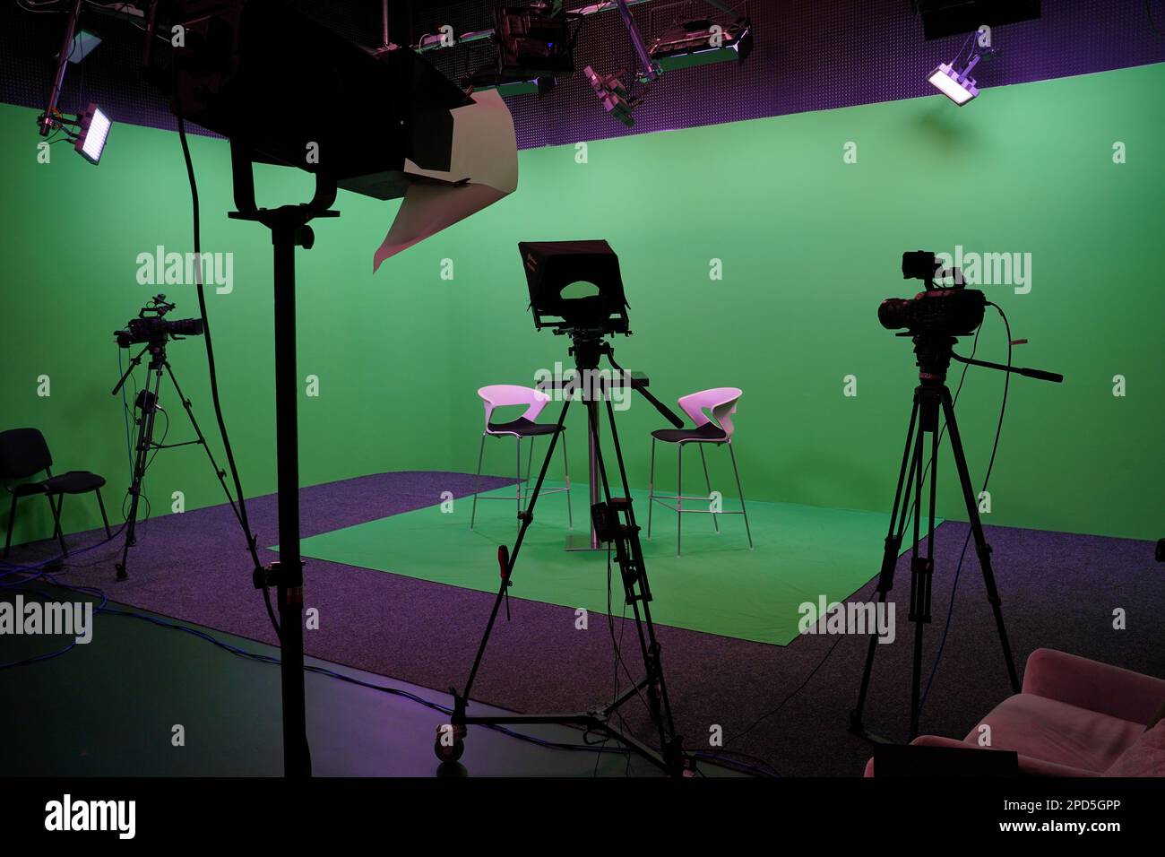 Moderne Einrichtung im Chroma Key Studio mit Fernseher, grünem Bildschirm, Licht, Kameraausstattung und Möbeln. Drehstudio mit professioneller Ausrüstung. Stockfoto