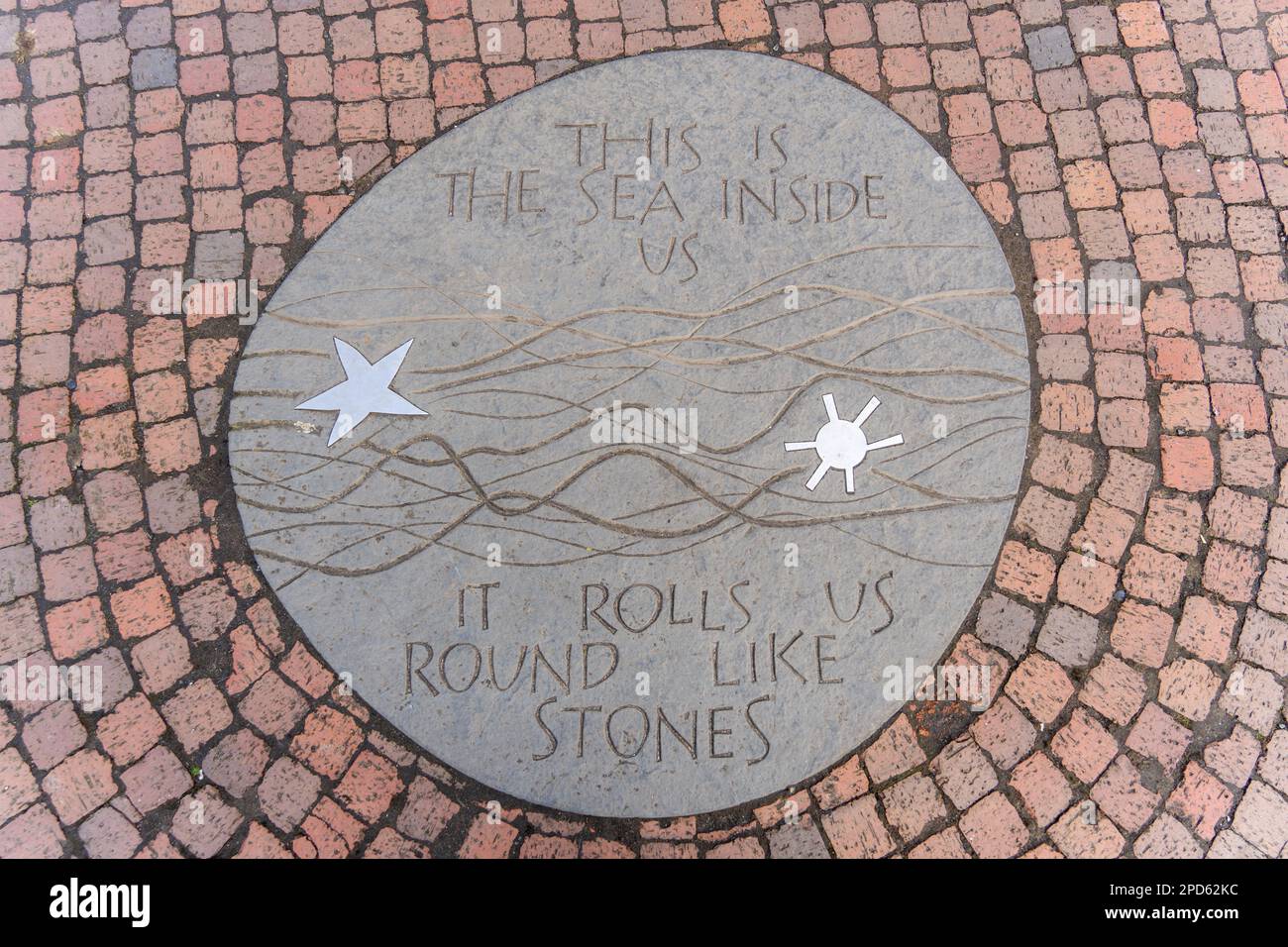 Auf einer Tafel auf dem Stadtplatz von Amble, Northumberland, Großbritannien, steht: „Dies ist das Meer in uns. Es rollt uns wie Steine." Stockfoto