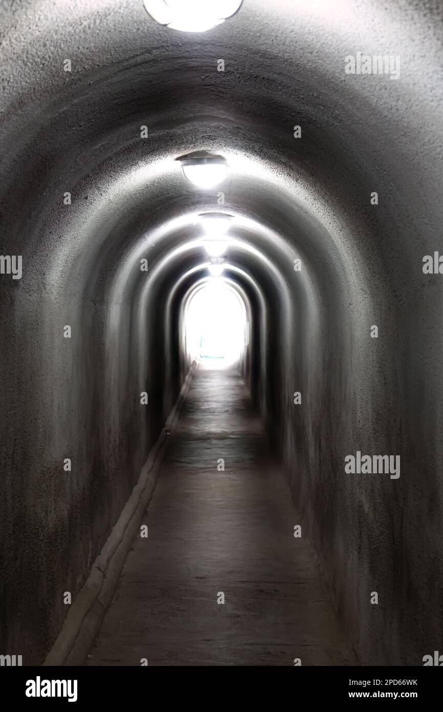 Langer Zementtunnel mit Lichtern an der Decke und Licht am Ende des Tunnels Stockfoto