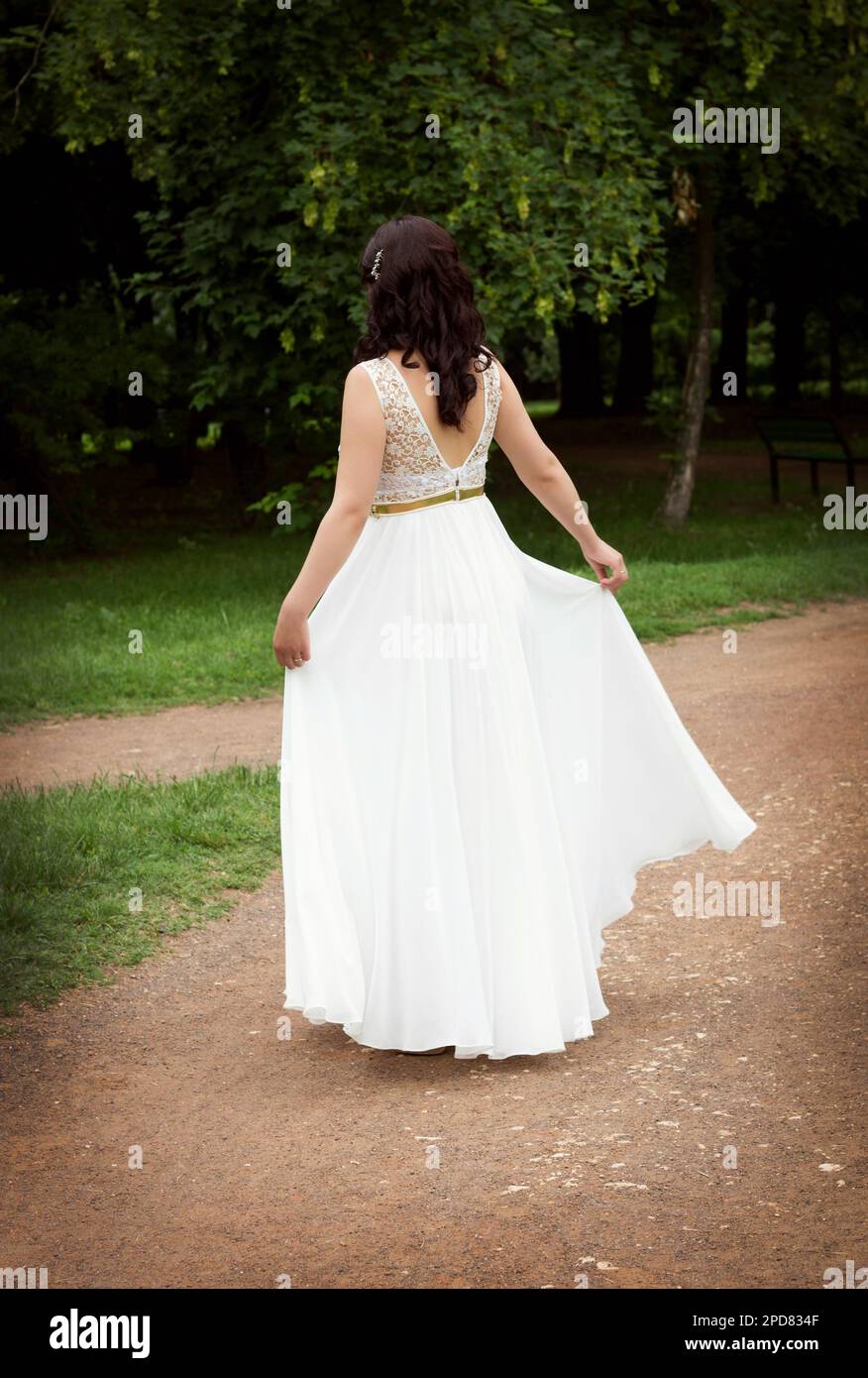 Braunes Mädchen steht in einem wunderschönen, weißen, langen Kleid mit tiefem Schnitt auf dem Rücken, in einem grünen Park Stockfoto