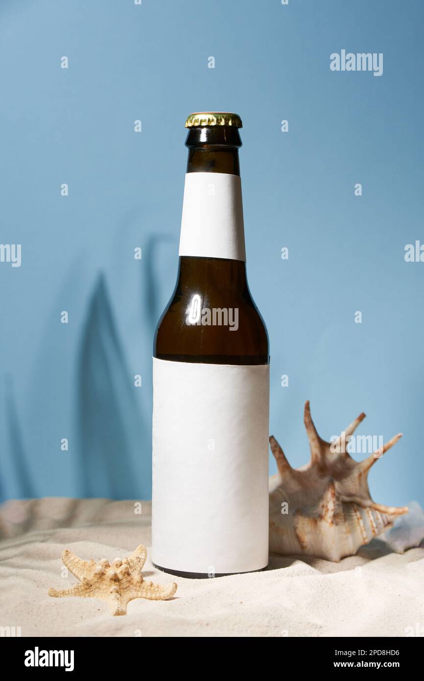 Eine Flasche Bier oder Ale mit Deckel steht im goldenen Sand mit Schalen. Kaltes Getränk für heißen Sommer Stockfoto