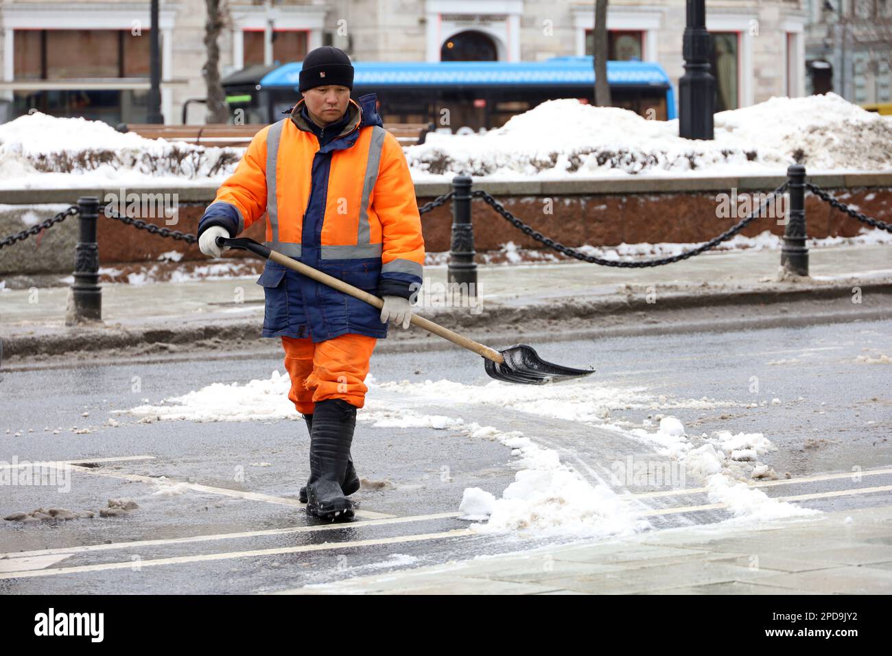 Ein asiatischer Arbeiter reinigt Schnee mit einer Schaufel auf der Stadtstraße. Straßenreinigung im Frühling Stockfoto