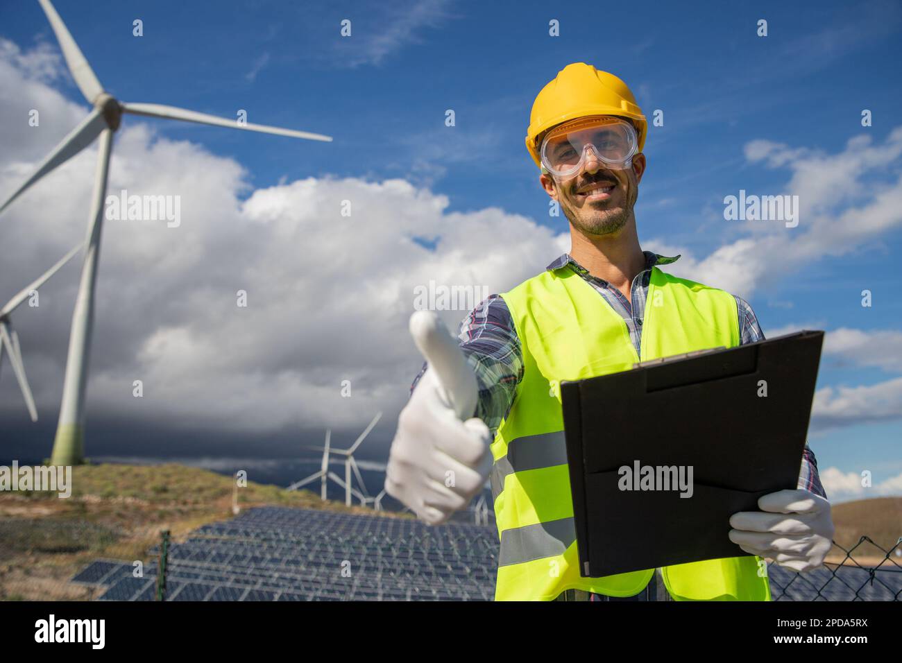 Ein lächelnder Ingenieur mit Daumen nach oben auf einer Solarfarm, erneuerbarer und nachhaltiger Energie Stockfoto