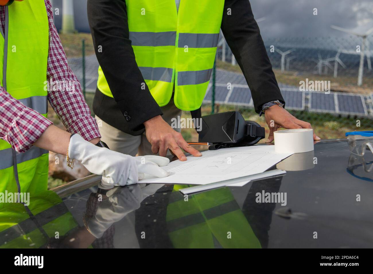 Nahaufnahme der Hände zweier Ingenieure, die eine technische Zeichnung eines Solarkraftwerks analysieren. Stockfoto