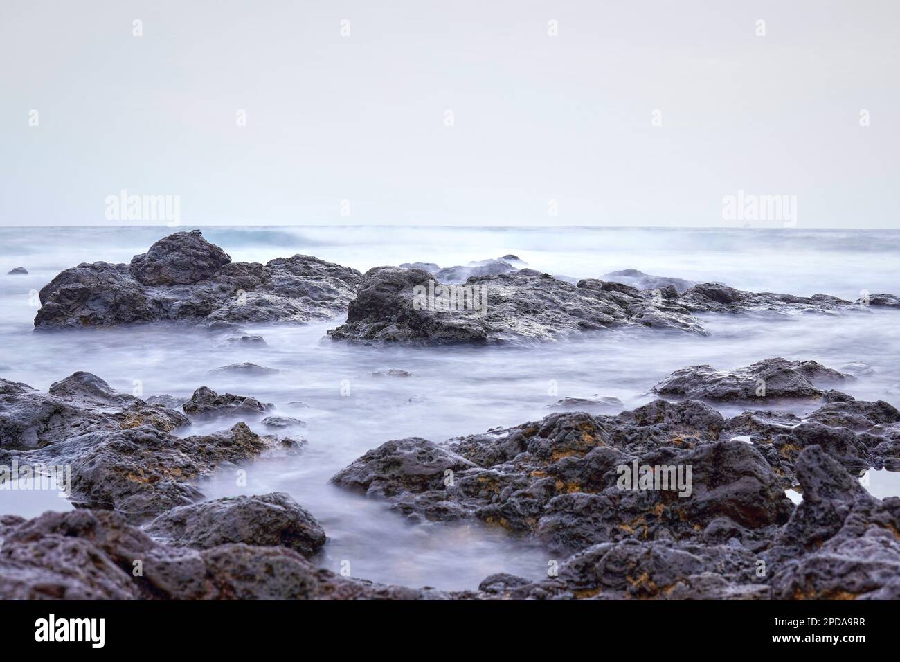 Wasser schwimmt um einige Felsen im Meer und bildet einen geheimnisvollen Nebel. Stockfoto