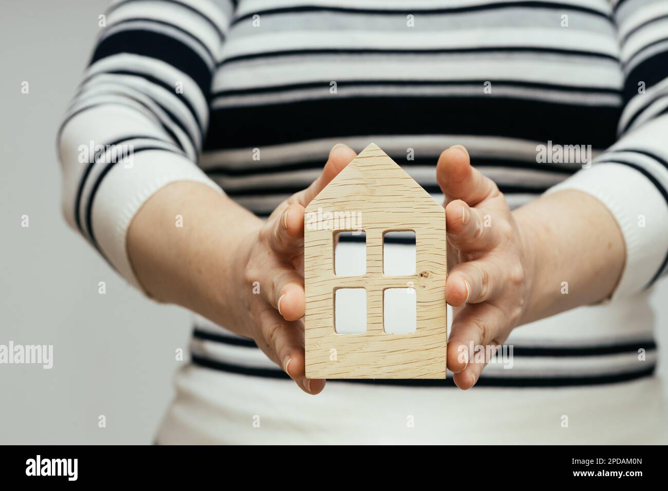 Eine Frau hält eine hölzerne Miniatur eines Hauses in ihren Händen, Wohnungskonzept, ein Haus bauen, eine Wohnung kaufen Stockfoto