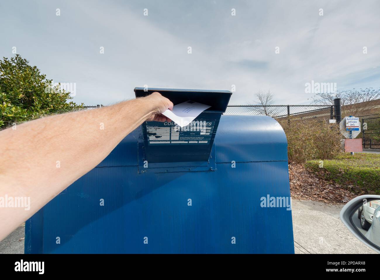 Horizontaler Schuss eines Mannes, der einen Brief in einen Briefkasten steckt. Stockfoto