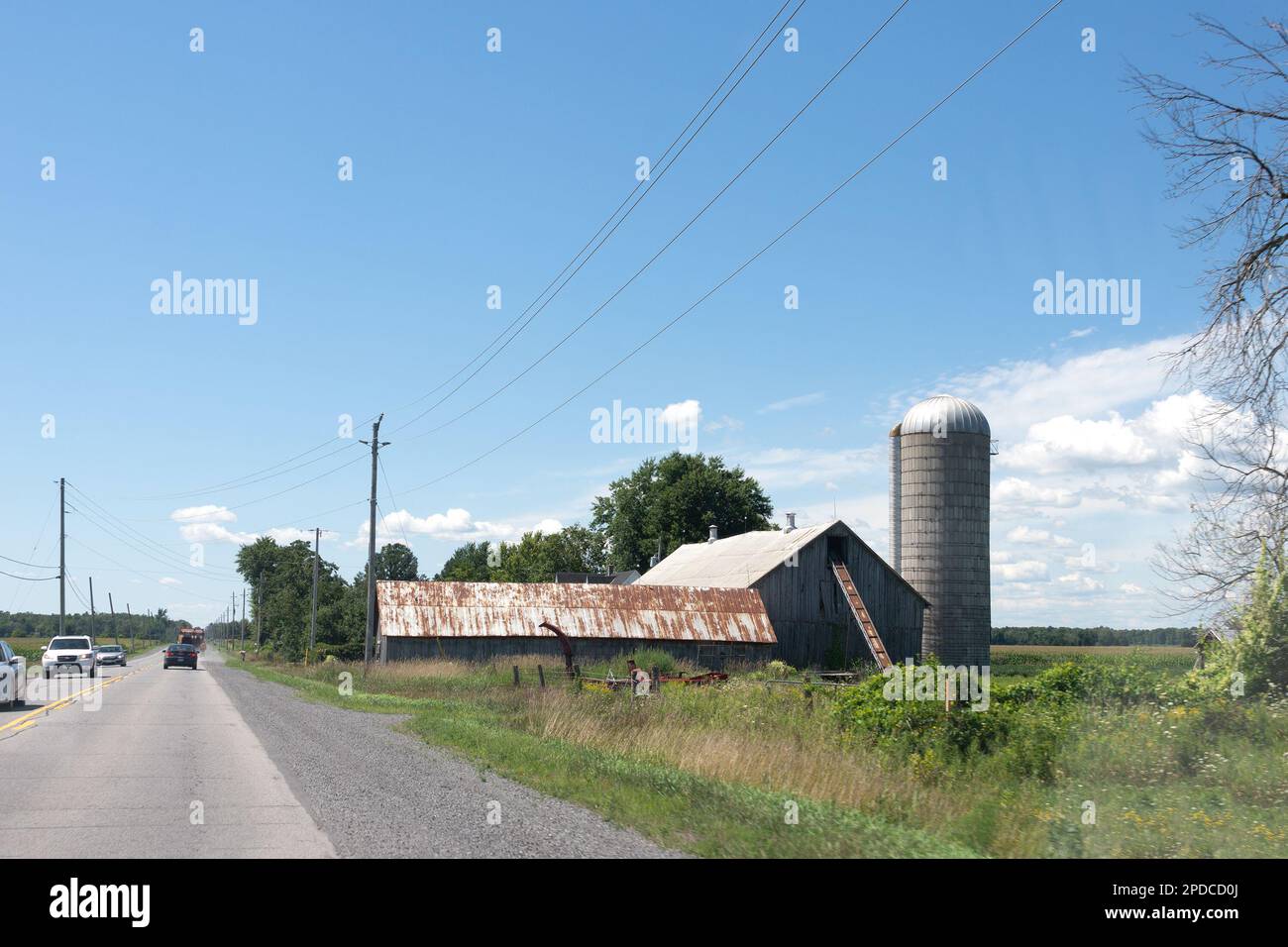 Verlassene Farm mit ungeschnittenem Gras in der Nähe der Straße, rostigen Dächern und einem Kornspeicher Stockfoto