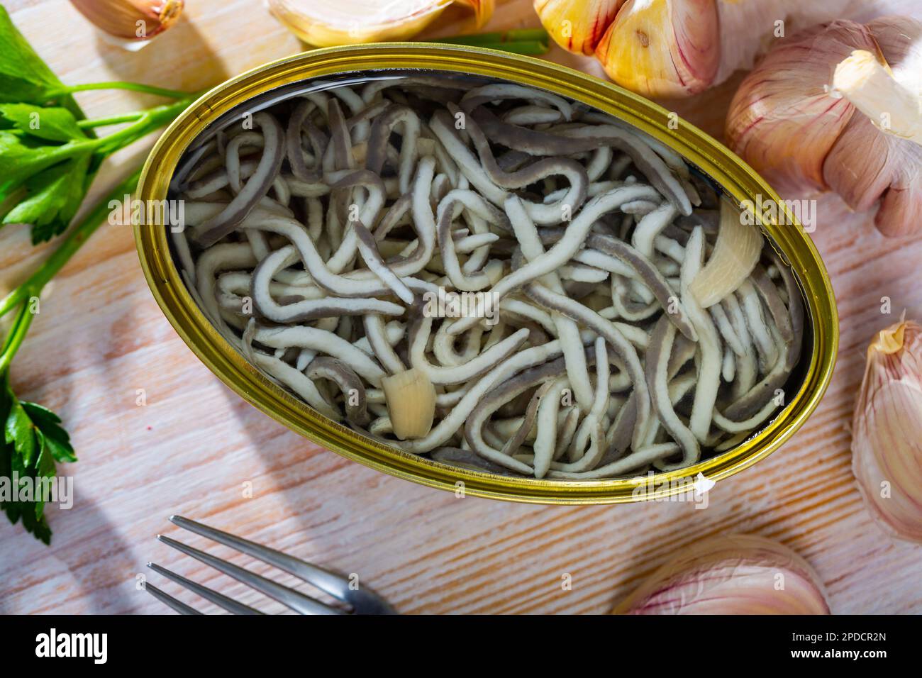 Offene Blechdose mit eingelegten Aalen und Knoblauch mit Gemüse am Tisch Stockfoto