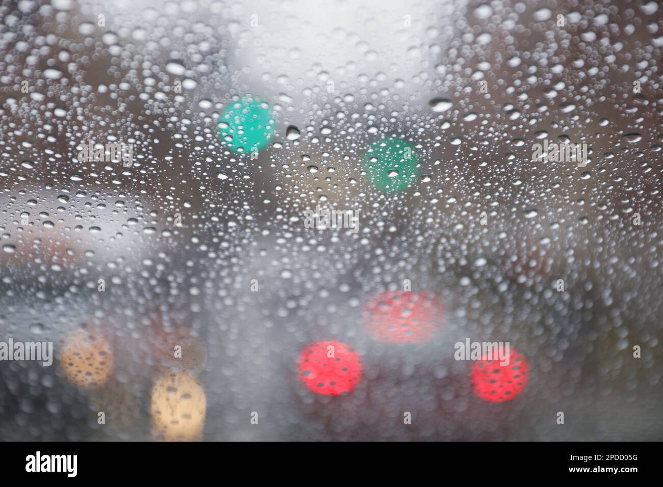 Regentropfen auf einem Fenster mit einer sanft verschwommenen Stadtlandschaft dahinter, die eine stimmungsvolle, atmosphärische Szene erzeugen. Ideal für Wetter, melancholische, gemütliche Momente in Innenräumen, Stockfoto