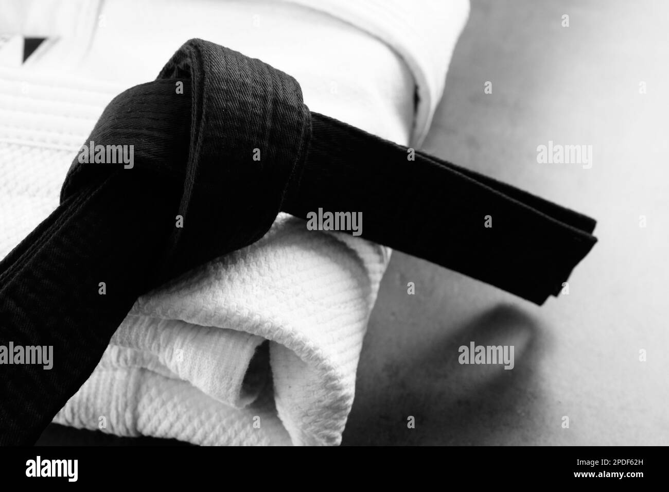Gefalteter weißer Kimono und schwarzer Gürtel auf grauem Steinhintergrund, Nahaufnahme Stockfoto