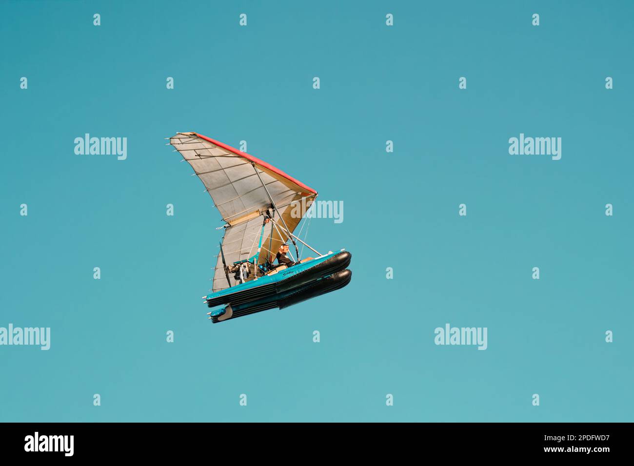 Ein älterer Mann, der mit der Hand in einem fliegenden Schlauchboot hallo sagt. Drachenfliegen Extremsport mit klarem blauem Himmel in Miami Stockfoto