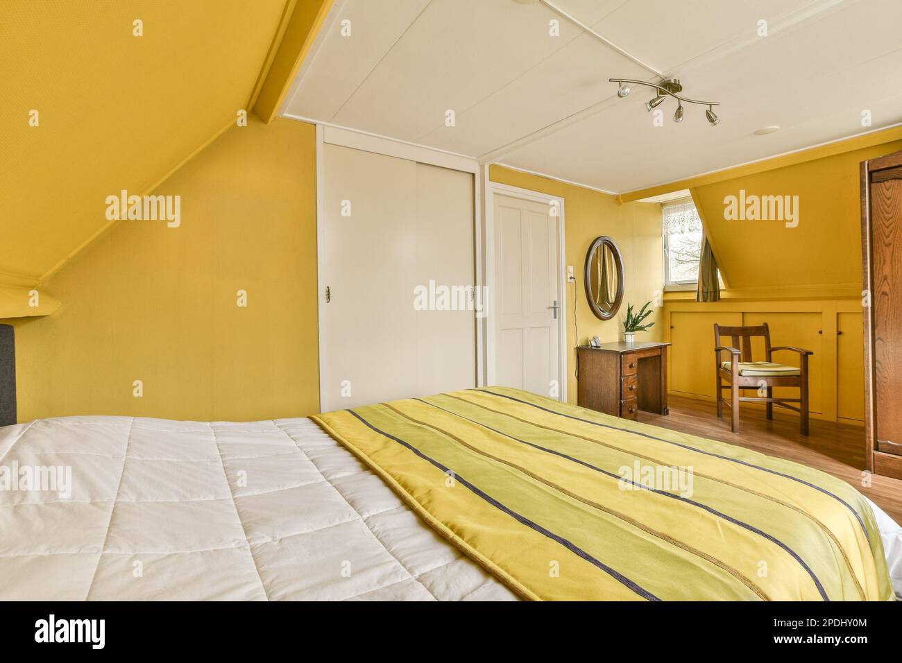 Ein Schlafzimmer mit Bett, Kommode und Spiegel an der Wand vor dem Zimmer sind hellgelbe Wände Stockfoto