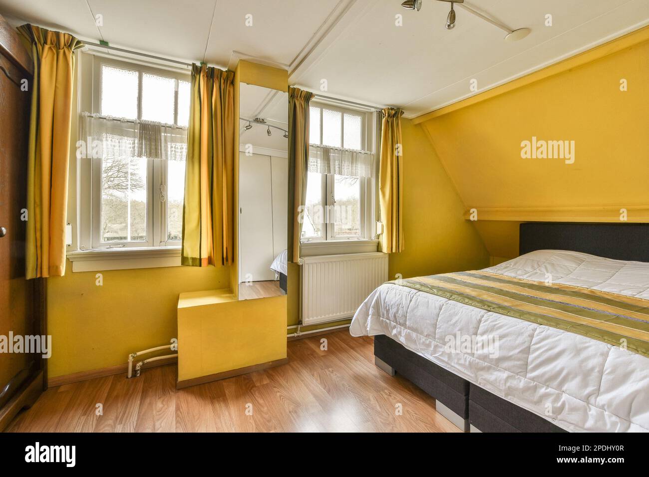 Ein Schlafzimmer mit gelben Wänden und Holzfußboden an der Wand, es gibt ein kleines Bett im Zimmer Stockfoto
