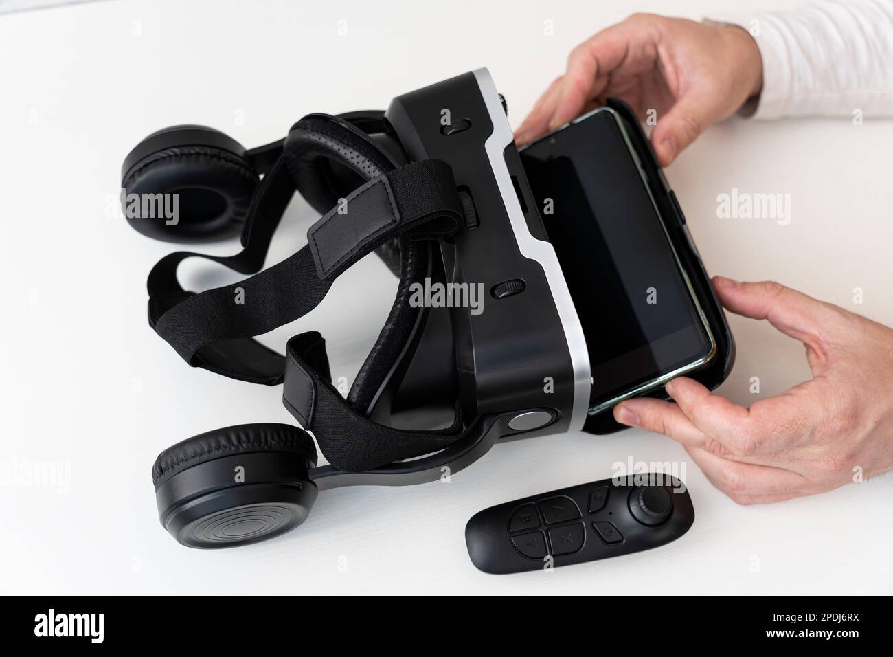 VR-Brille und Smartphone mit Beschneidungspfad für Bildschirm auf weißem Hintergrund. Die Hände von Männern stecken ein Smartphone in eine VR-Brille. Stockfoto