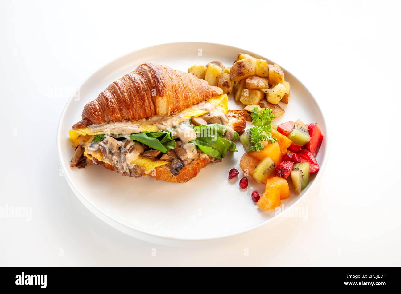 Mediterranes Rührei-Croissant-Sandwich mit Obst und Kartoffeln. Stockfoto