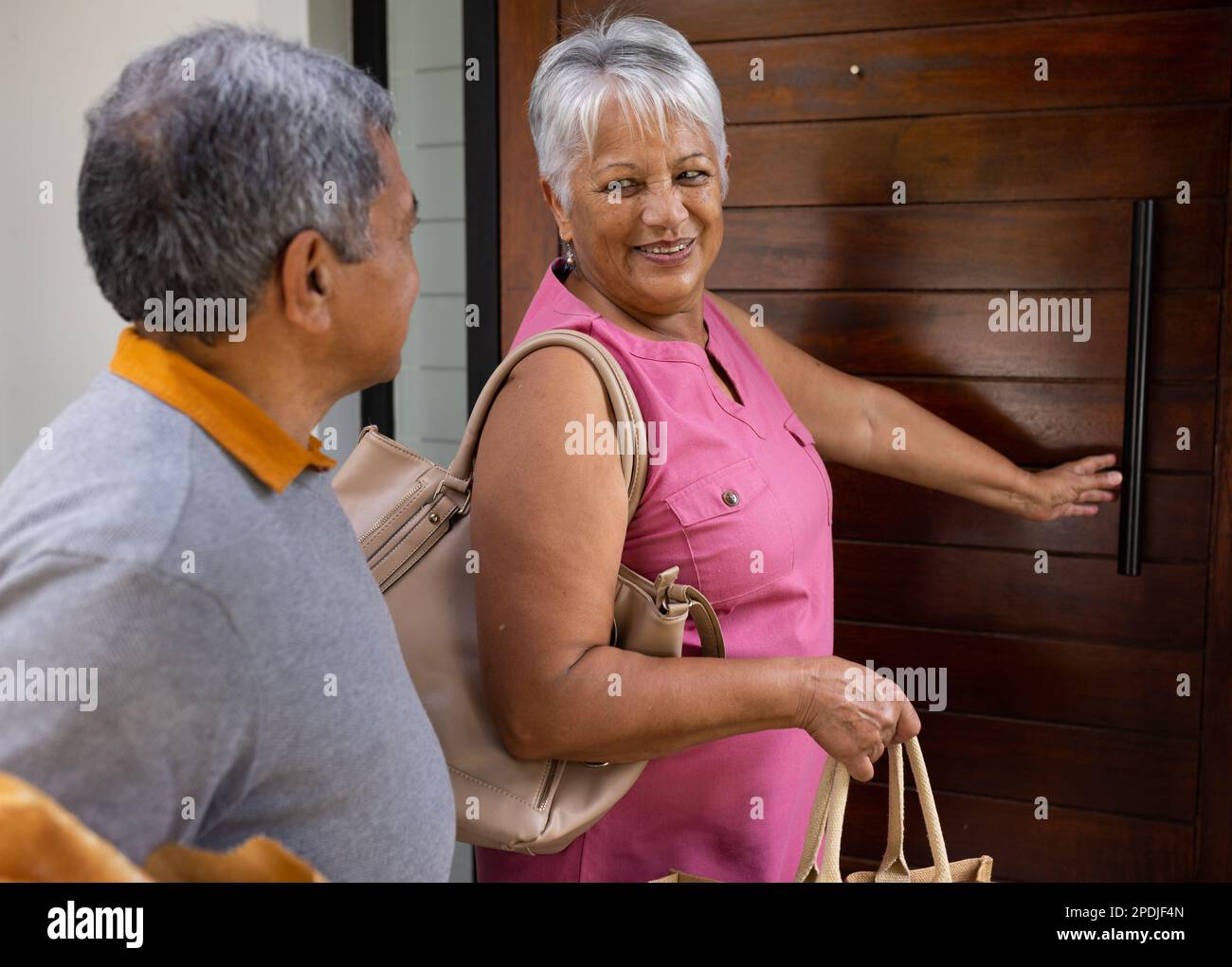 Lächelnde, birassistische Seniorin, die ihren Mann ansieht, während sie vor dem Haus an einer verschlossenen Tür steht Stockfoto