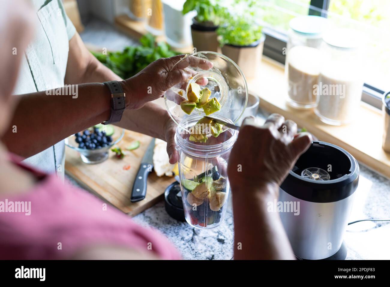 Die Mitte des zweirassistischen Seniorenpaares, das Fruchtscheiben in den Mixer legt, während er Smoothie in der Küche macht Stockfoto