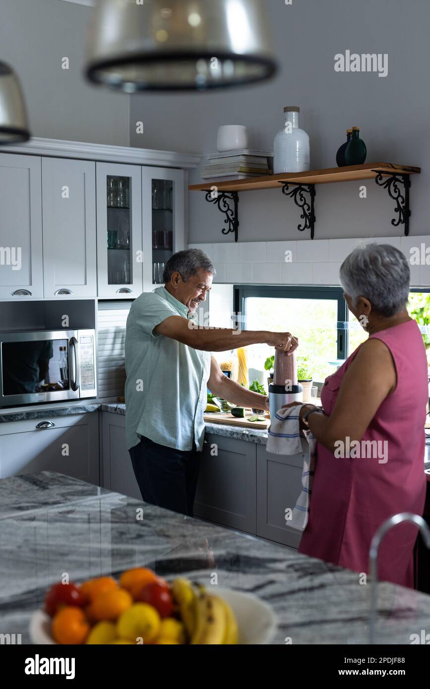 Birassische Seniorin, die einen Ehemann anschaut, der Smoothie auf der Küchentheke zuhause mixt, Kopierraum Stockfoto