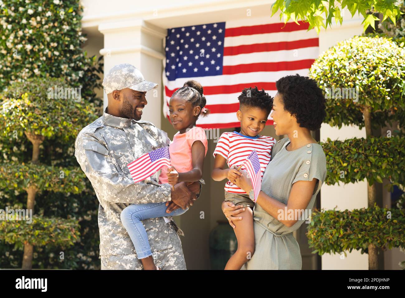 Ein glücklicher afroamerikanischer Soldat und seine Familie umarmen sich und halten usa-Flaggen Stockfoto