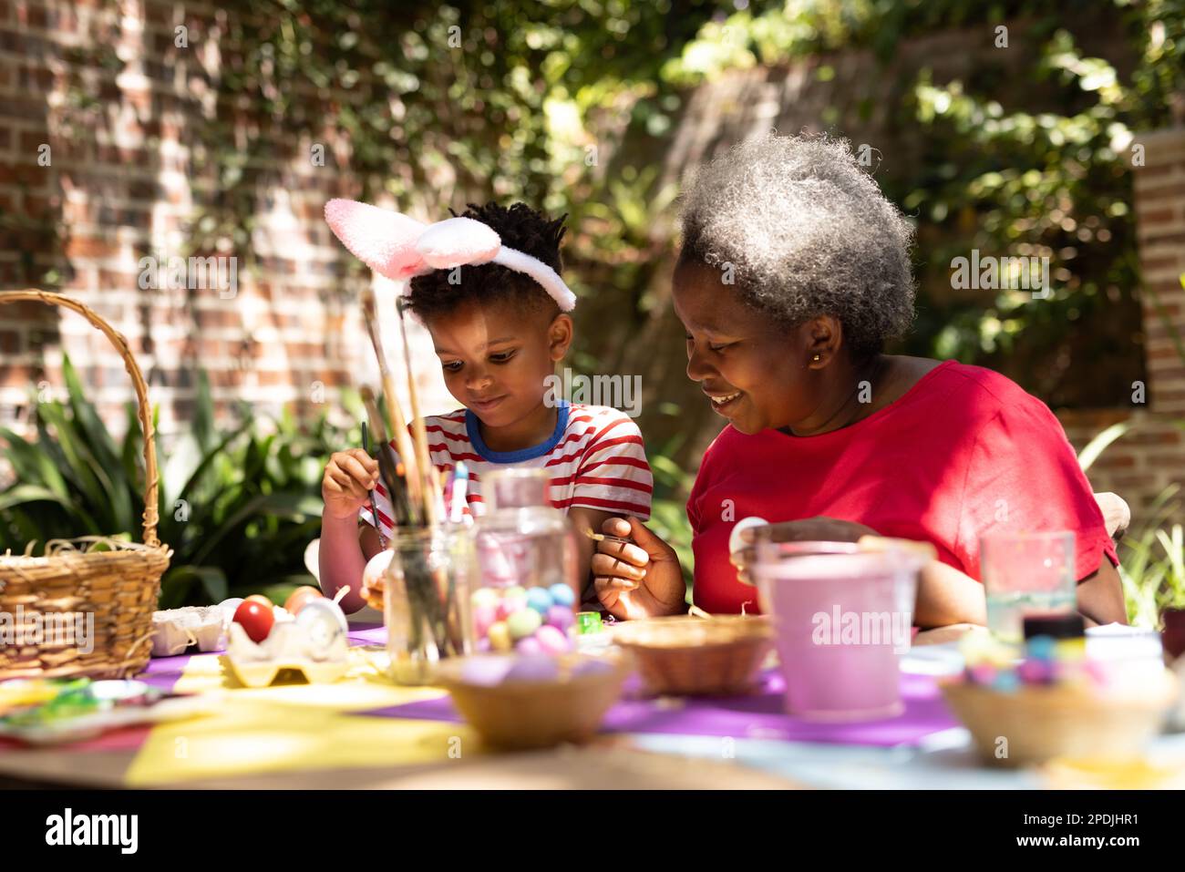 Frohe afroamerikanische Großmutter und Enkel, die ostereier im Garten färbten Stockfoto
