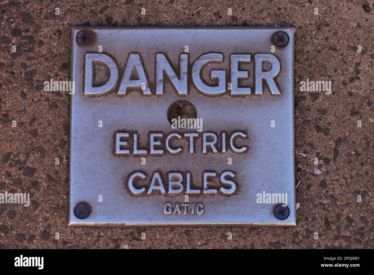 Warnschild „Gefahr durch Elektrizität“ mit Warnung vor elektrischen Kabeln auf einer quadratischen Metalloberfläche mit Betonhintergrund. Stockfoto