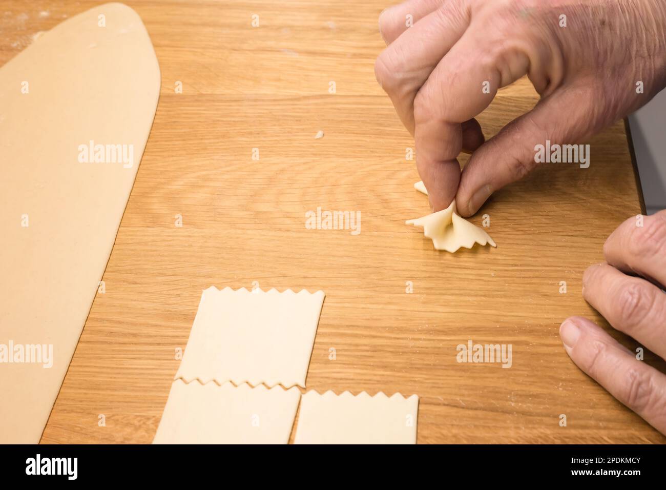 Herstellung hausgemachter Nudeln – italienische Nudeln (Farfalle) in heimwerkerarbeit – Nahaufnahme einer Hand, die den Teig zur Zubereitung selbstgemachter Farfalle-Nudeln presst Stockfoto