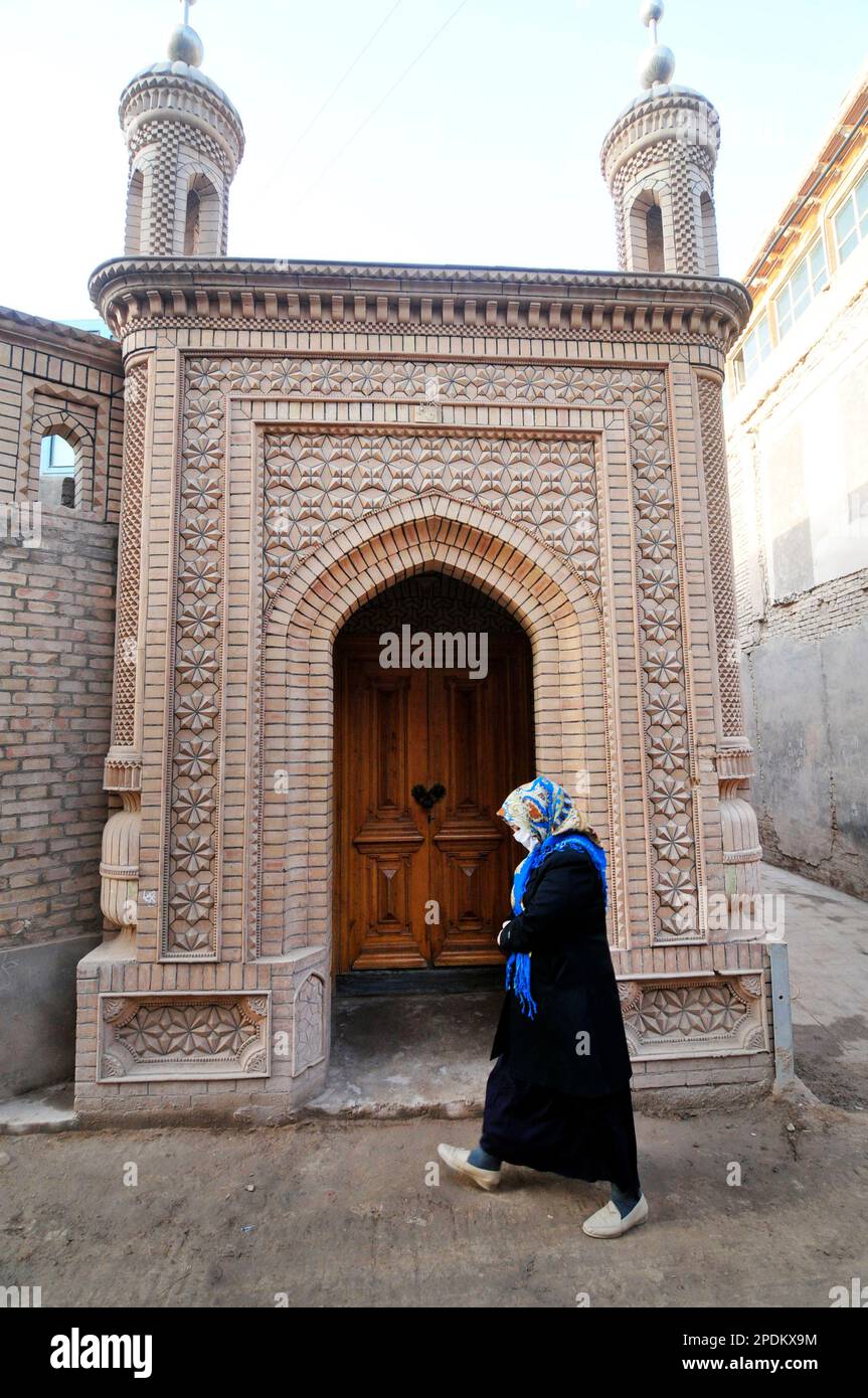 Eine uigurische Frau, die an einer kleinen Moschee in der Altstadt von Kashgar, Xinjiang, China vorbeigeht. Stockfoto